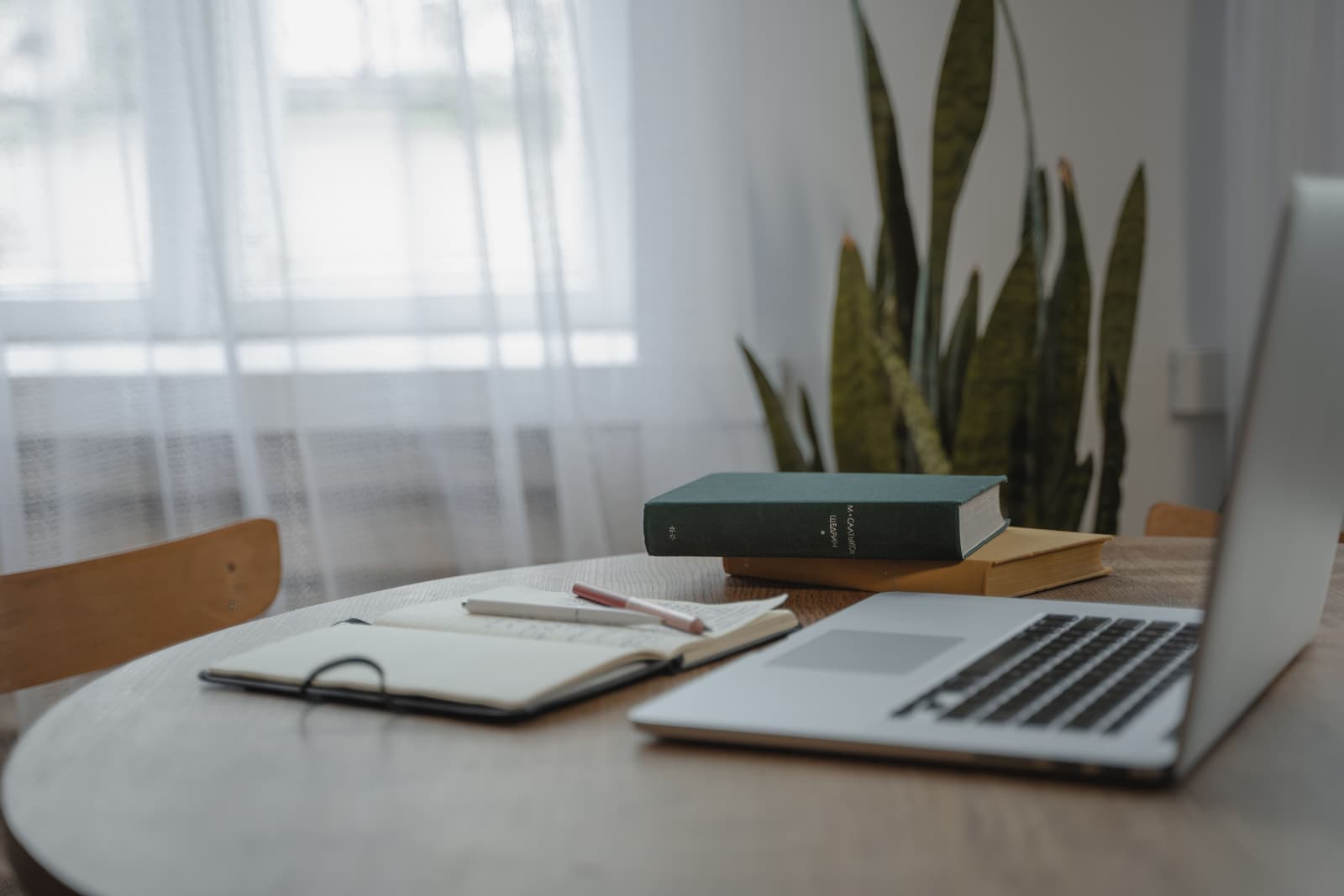 A table with a laptop, books and an open notebook, ready to sit down at.