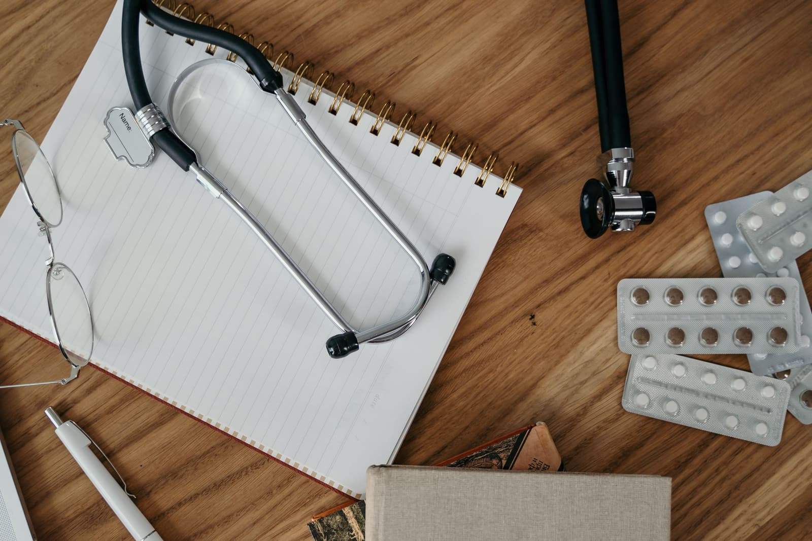 A stethoscope, notebook and reading glasses on a wooden desk.