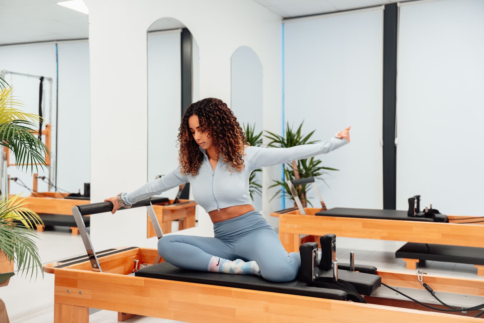 A woman moving on a studio reformer, with arched mirrors behind her.